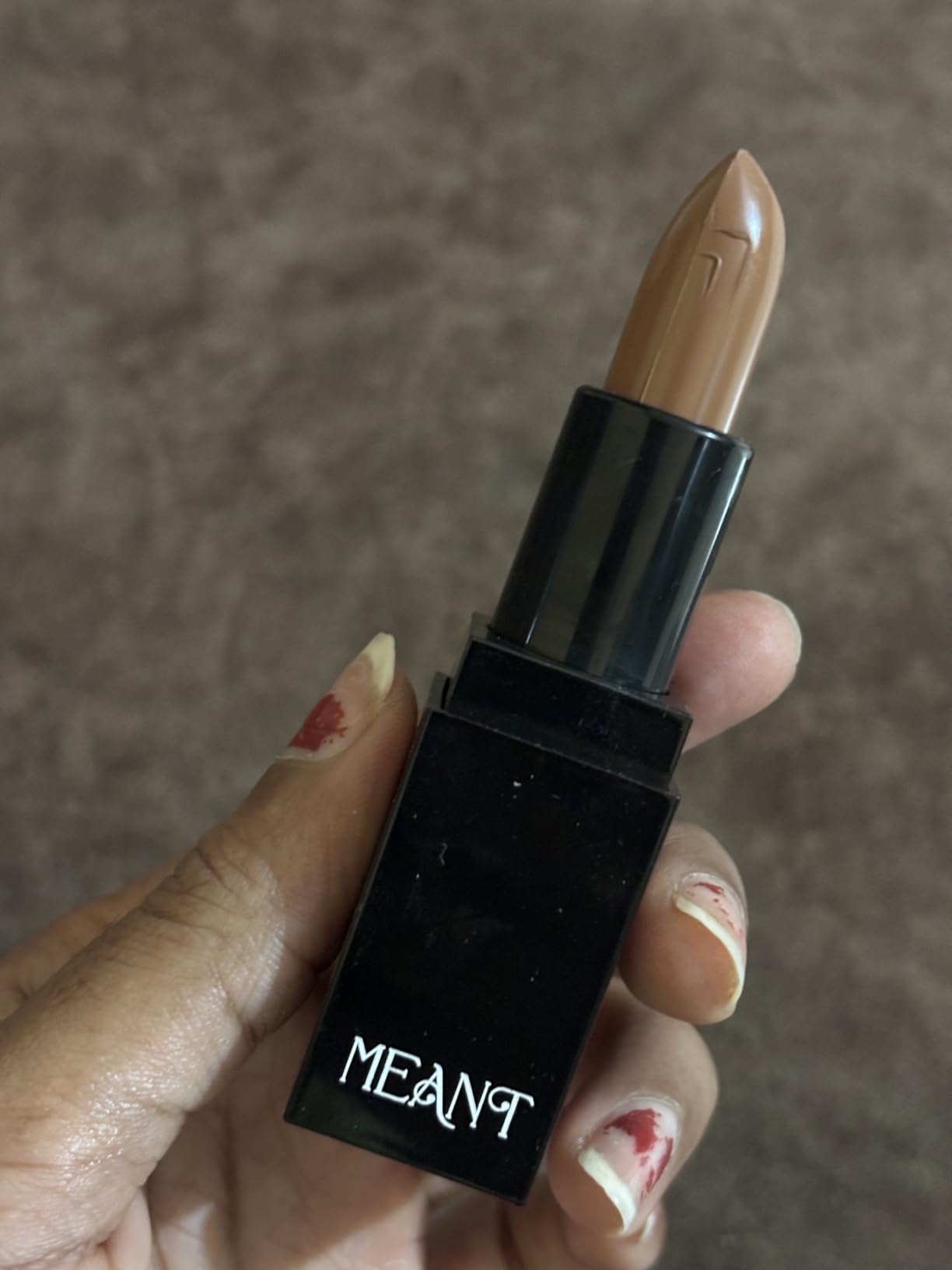 MEANT's Silky Swipe Amber Aura Lipstick held by hand against a neutral background