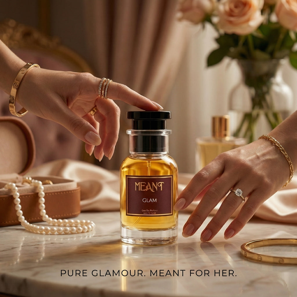 Female hand holding perfume bottle labeled 'MEANT Glam' with decorative items in the background.